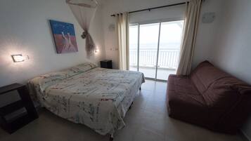A bedroom with a bed, a nightstand, a sofa, a window with curtains, and a painting on the wall.
