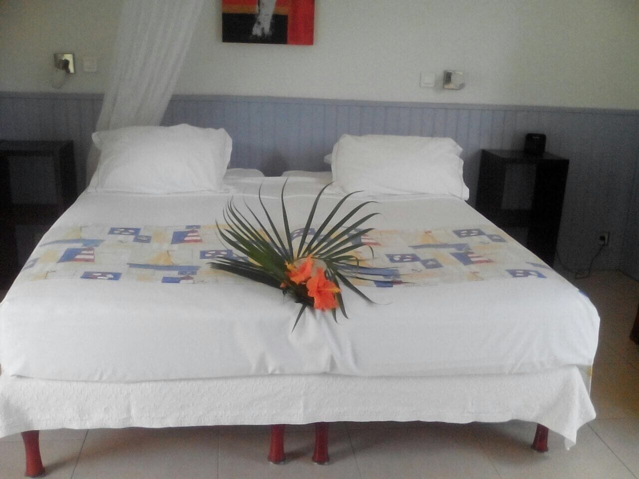 Una cama bien tendida con un centro de mesa floral, ropa de cama blanca y un cabecero a rayas.