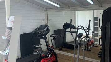 Un gimnasio con equipo de ejercicio que incluye una bicicleta de spinning, una elíptica y pesas.
