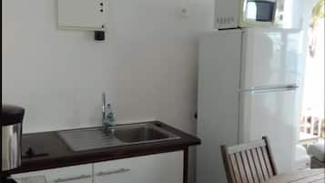 A compact kitchen with white cabinets, a stainless steel sink, a microwave, and a refrigerator.