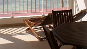 Un espace extérieur abrité, aménagé avec des tables et des chaises en bois, offrant une vue sur l’océan et agrémenté d’un palmier.
