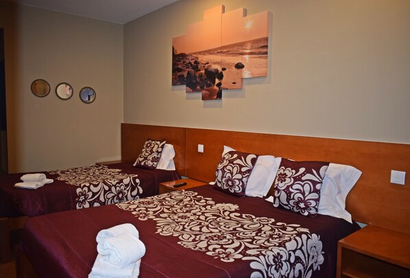 A hotel room with two beds, each with a patterned bedspread and pillows, a wall-mounted artwork depicting a beach scene, and three round mirrors on the wall. - Residencial Belo Horizonte (Porto)