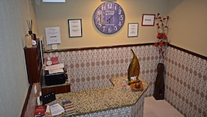 A hotel reception area with a clock, framed certificates, and a decorative vase.