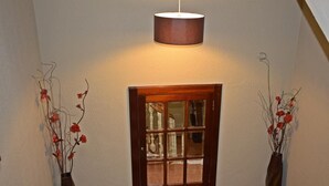 A hallway with a wooden-framed window, two vases with dried flowers, and a hanging light fixture.