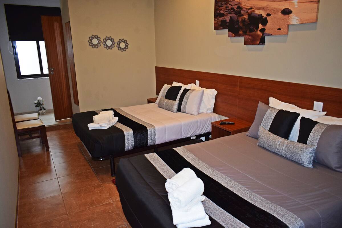 Hotelkamer met twee bedden, een houten hoofdbord, een klein tafeltje en een wand met decoratieve spiegels en een foto.