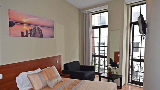 A hotel room with a bed, a chair, a small table, and a TV mounted on the wall.