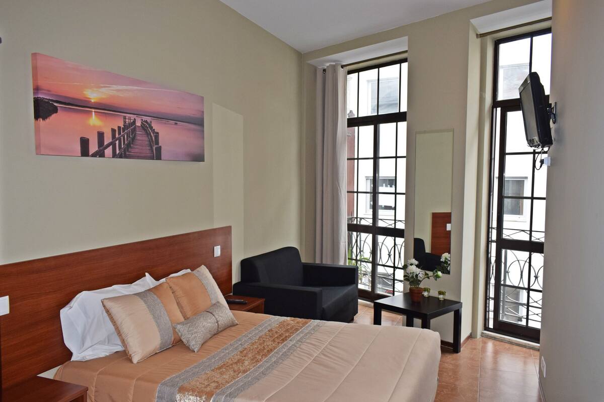 Een hotelkamer met een bed, een stoel, een klein tafeltje en een tv aan de muur.