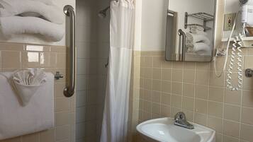 Une salle de bain avec une douche, un lavabo et un miroir. Des serviettes et un sèche-cheveux sont accrochés au mur.