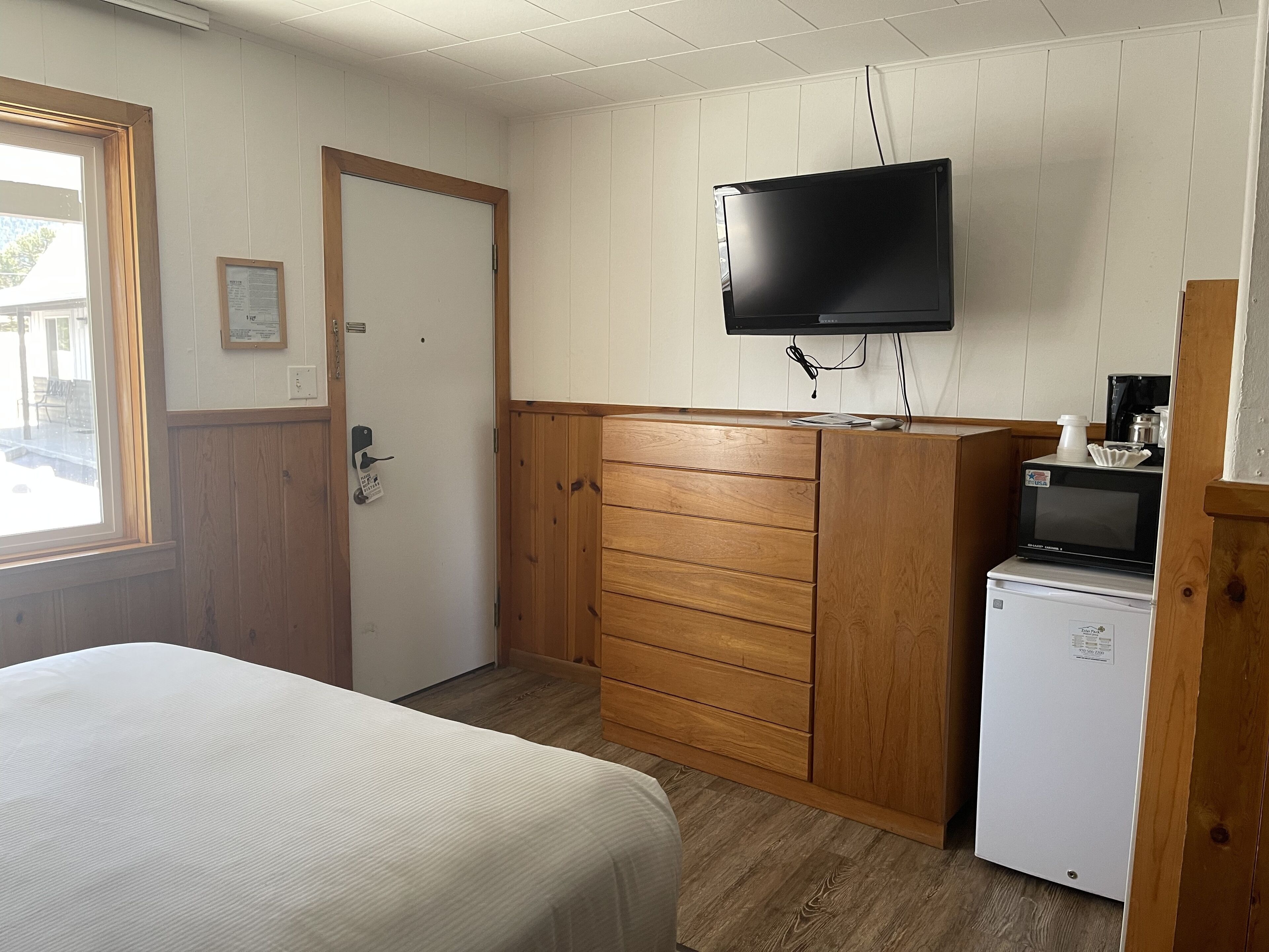 Ein Hotelzimmer mit Bett, Holzschrank, einem an der Wand befestigten Fernseher und einem kleinen Kühlschrank.