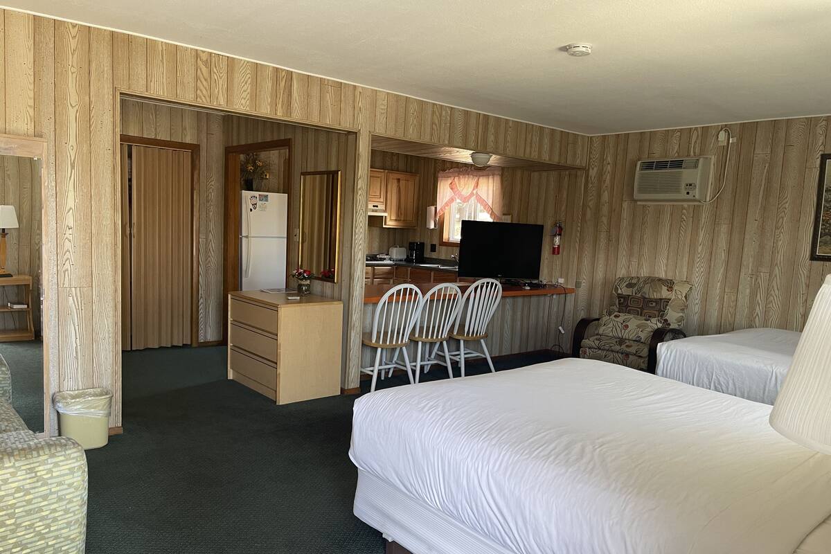 A hotel room with two beds, a kitchenette, a desk, and a chair.