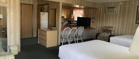Ein Hotelzimmer mit zwei Betten, einer Küchenzeile, einem Schreibtisch und einem Stuhl.