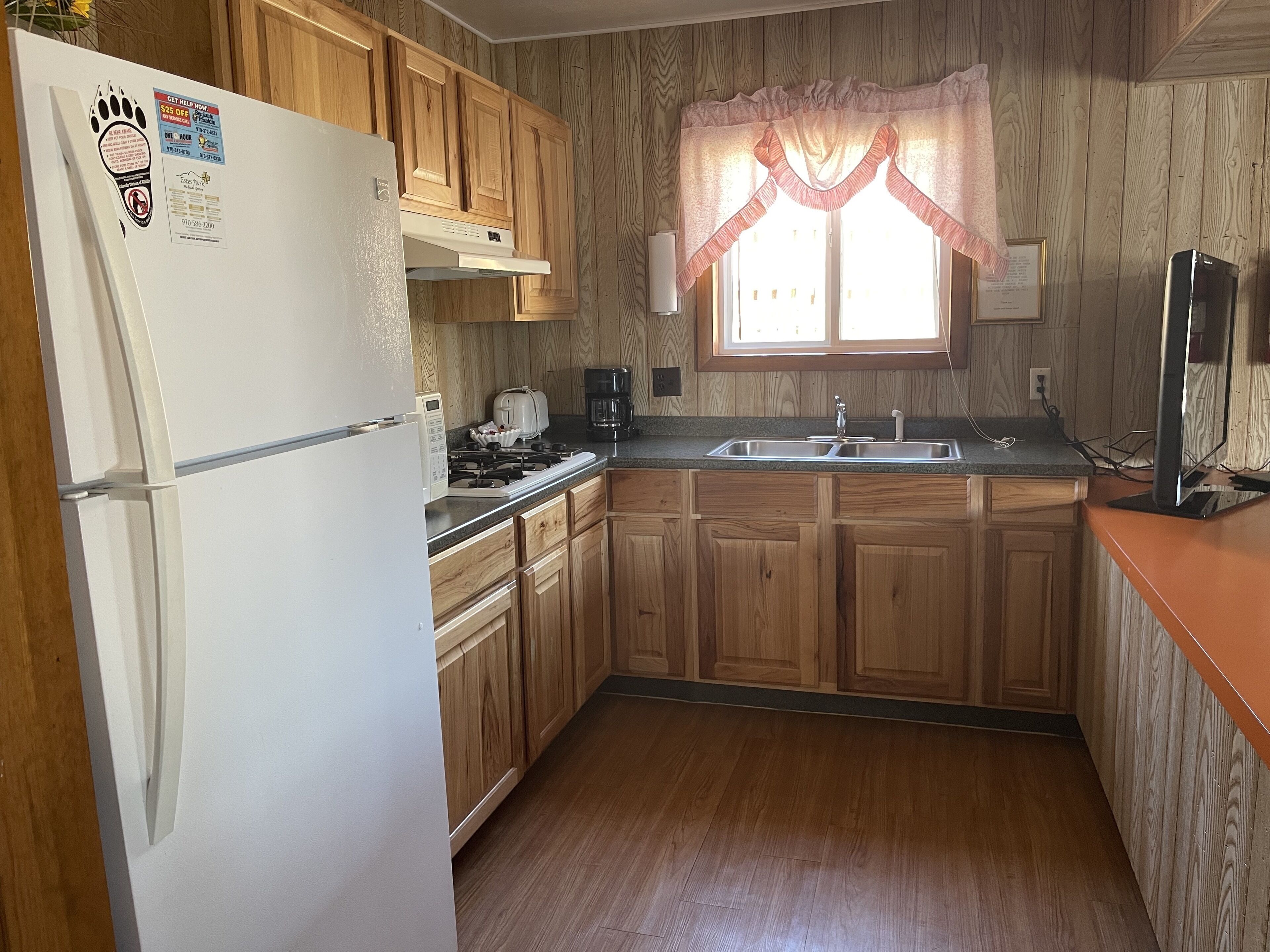 A kitchen with wooden cabinets, a refrigerator, a stove, and a window with a decorative valance.