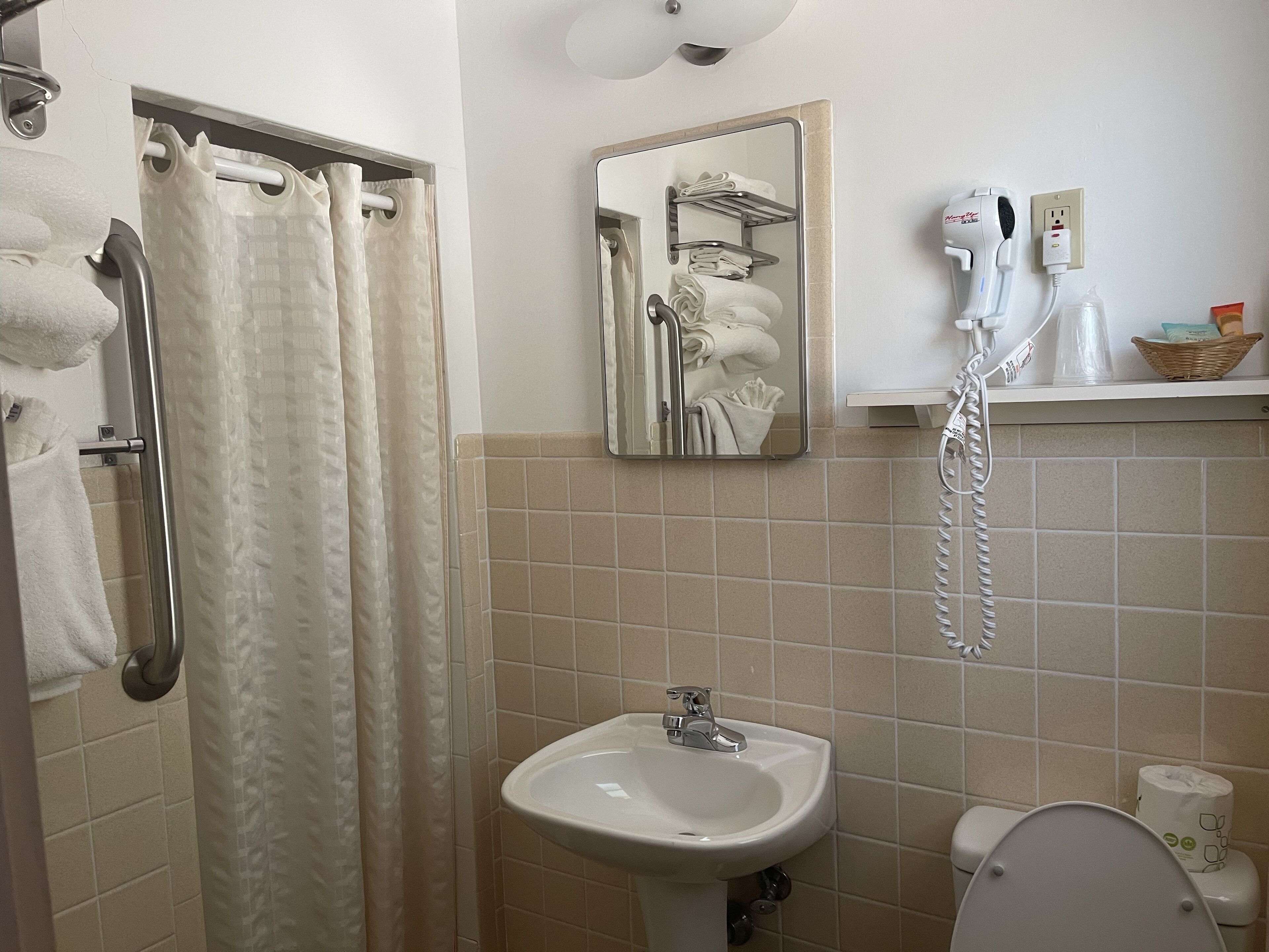 Un baño con ducha, lavamanos, inodoro, toallero y secador de pelo.