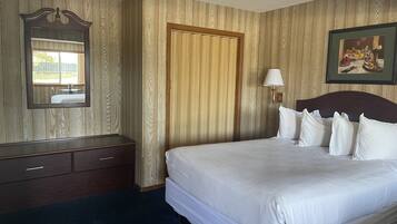 A hotel room with a large bed, a wooden wardrobe, a mirror, a door, and a framed picture on the wall.