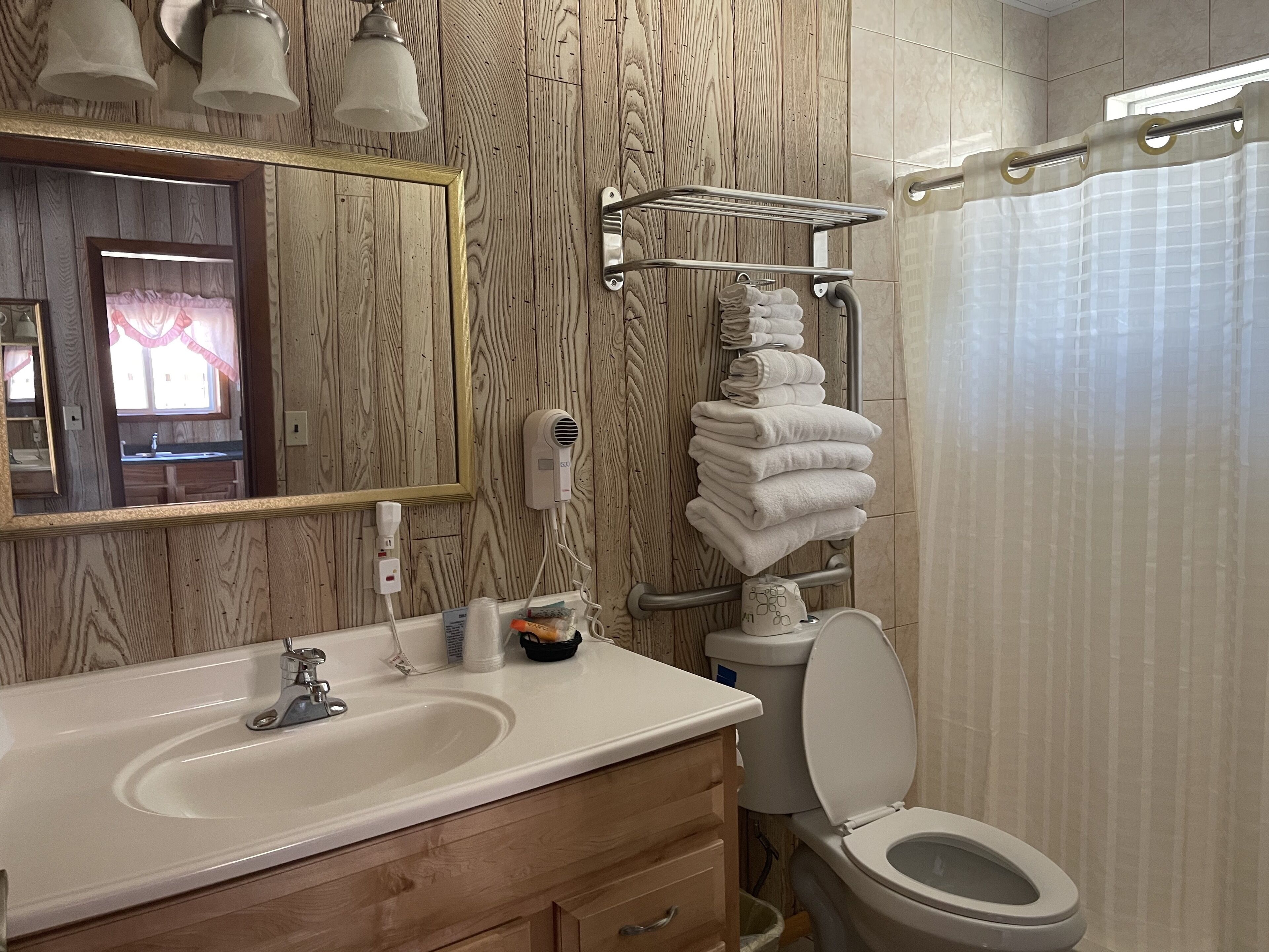 A bathroom with a wooden wall, a sink, a toilet, a towel rack, and a mirror.