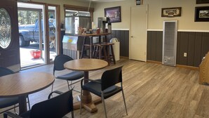 Een restaurantinterieur met ronde tafels en stoelen, een koffieapparaat en een televisie aan de muur.