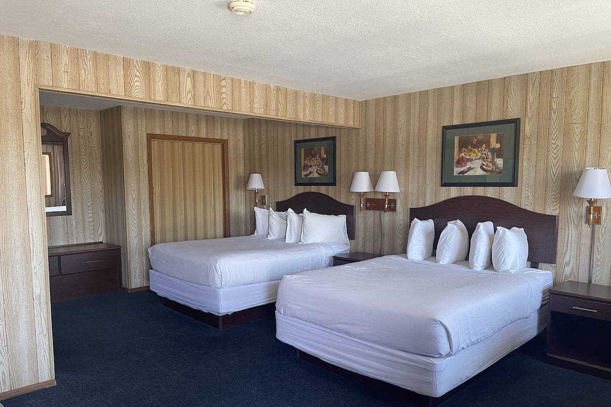 A hotel room with two beds, a dresser, a mirror, and two wall-mounted lamps.