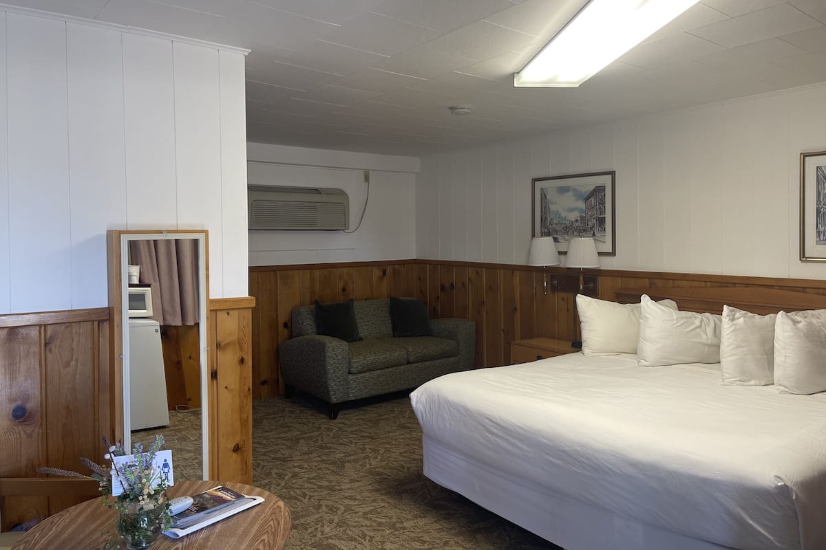 A hotel room with a bed, a wooden headboard, a small couch, a table with a vase of flowers, and a framed picture on the wall.