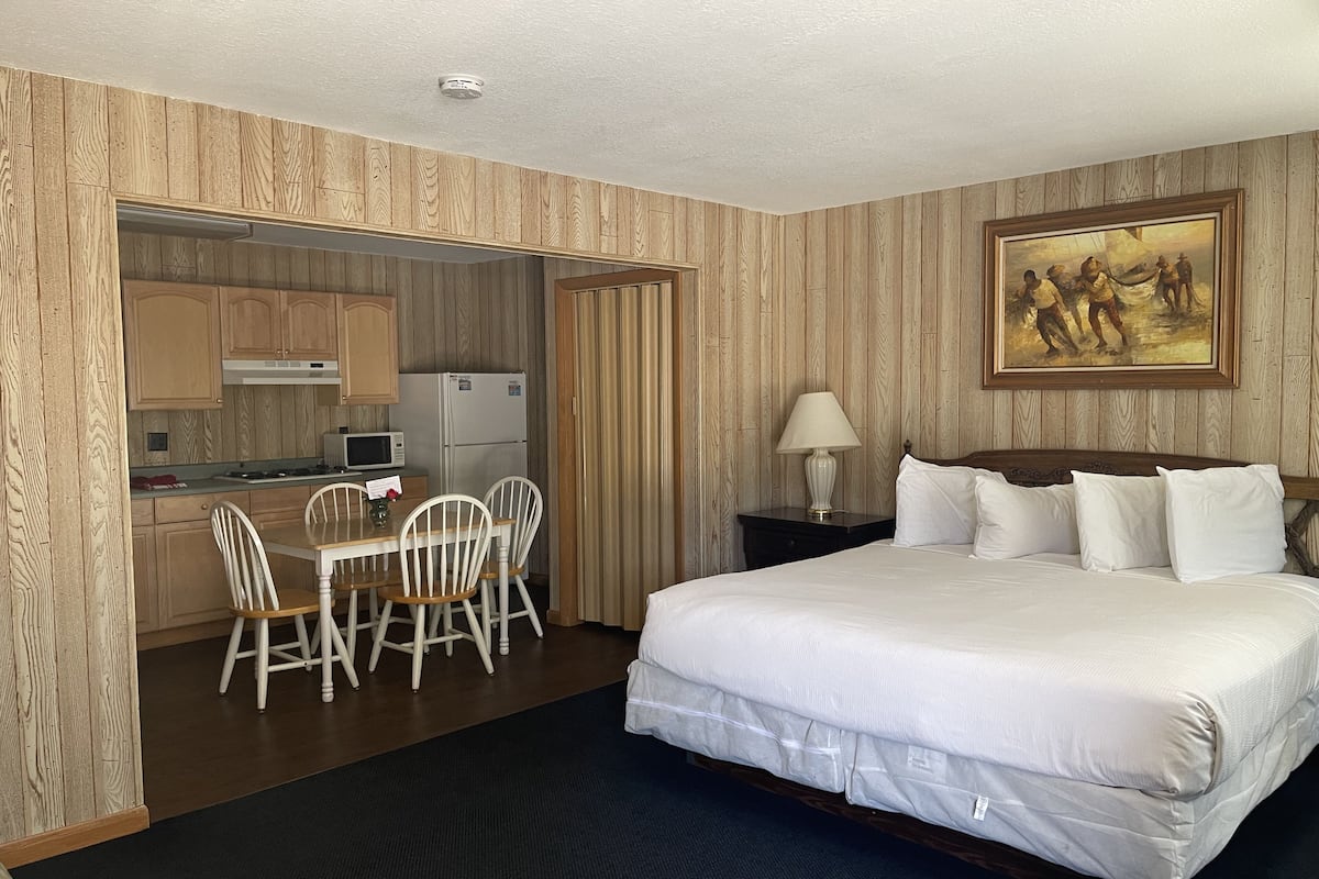 A hotel room with a bed, a desk with chairs, a microwave, and a refrigerator.