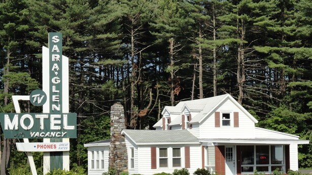 A motel with a stone chimney, a TV sign, and a sign indicating vacancy.