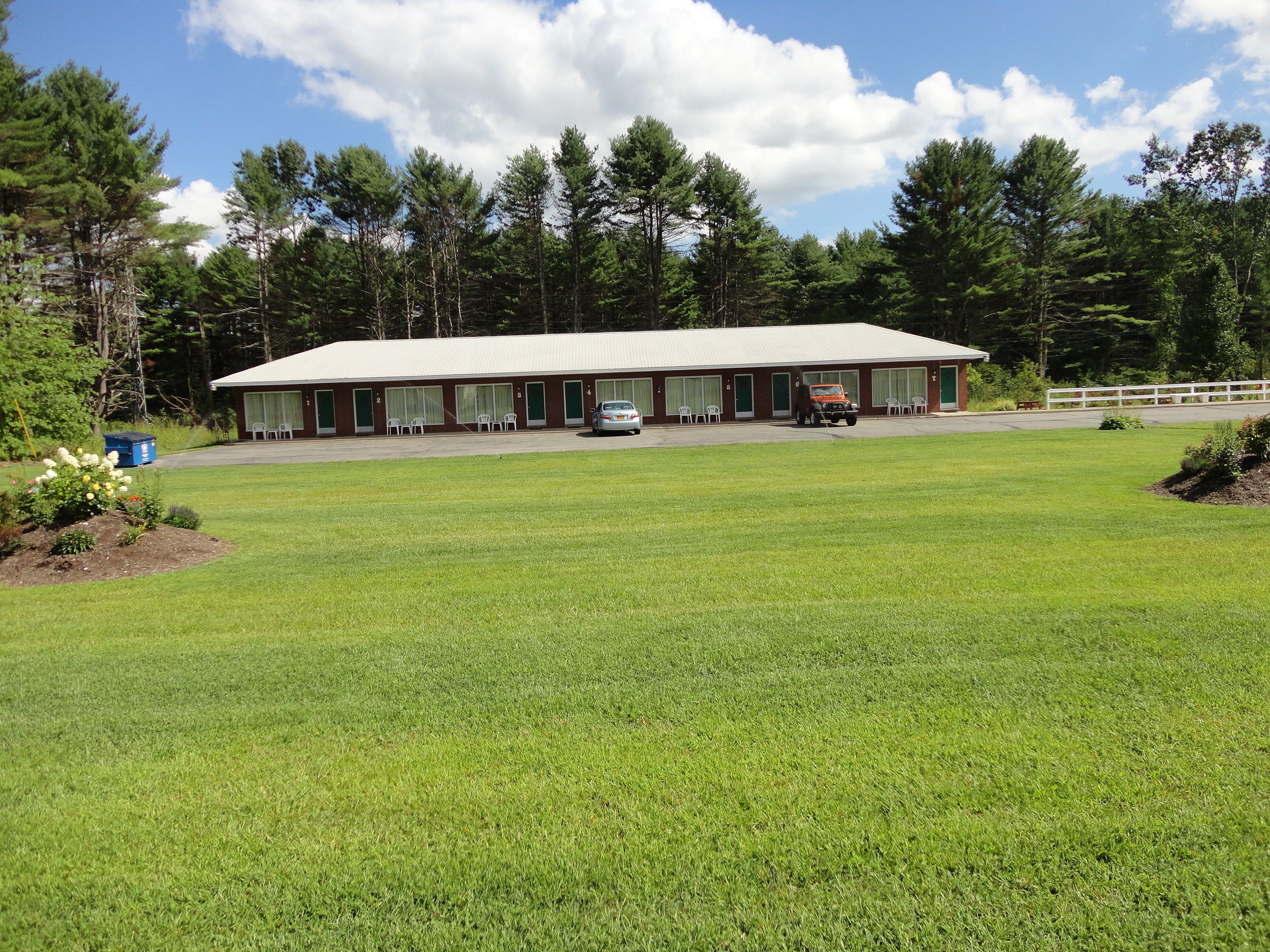 A motel with a large lawn, a parking area, and a row of rooms with windows.
