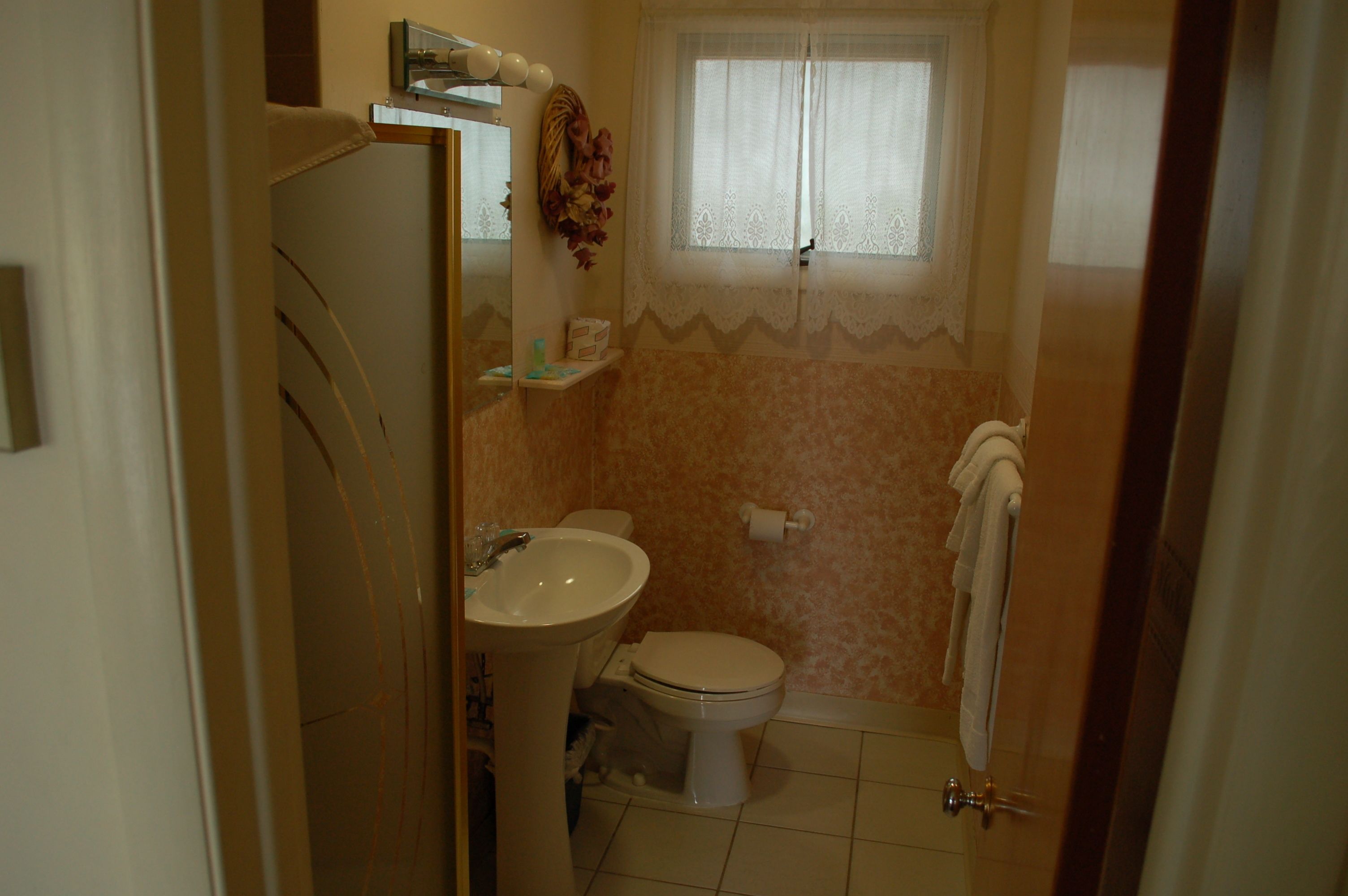 Une salle de bain avec des toilettes, un lavabo et une fenêtre ornée de rideaux en dentelle.
