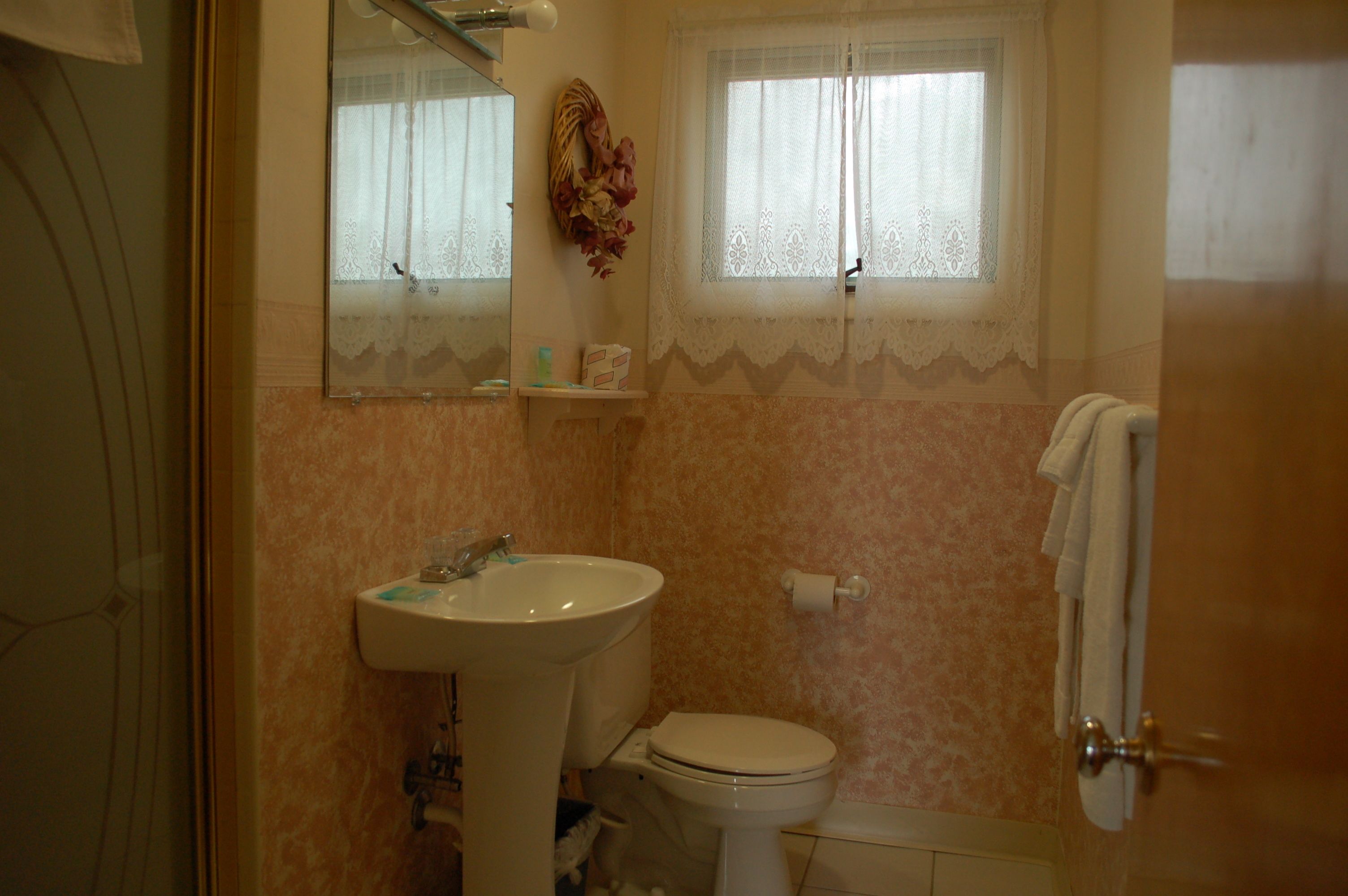 A bathroom with a sink, toilet, and a window with lace curtains.