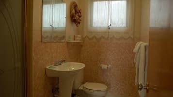 A bathroom with a sink, toilet, and a window with lace curtains.