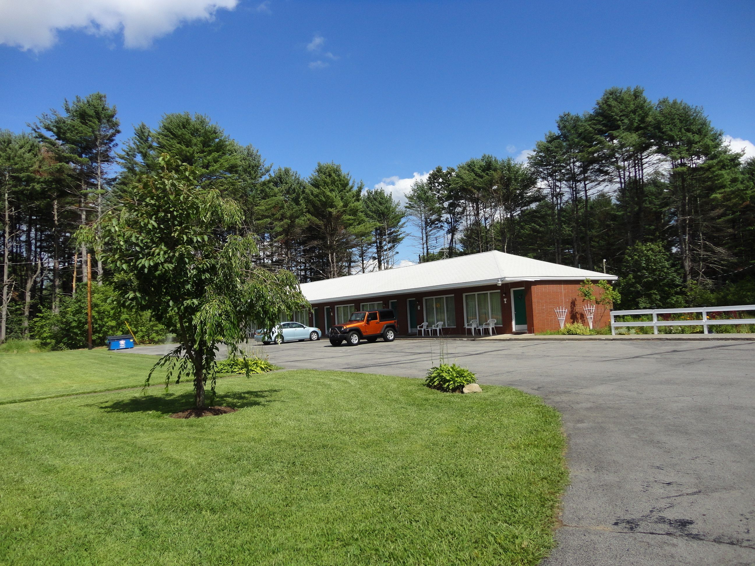 A building with a white roof and brick walls, surrounded by trees and a grassy area.