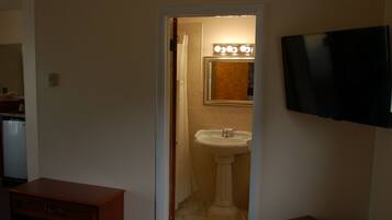 A bathroom with a pedestal sink, a mirror with lights, a television on the wall, and a wooden cabinet.