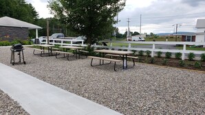A picnic area with benches and a grill, a white fence, and a motel sign in the background.