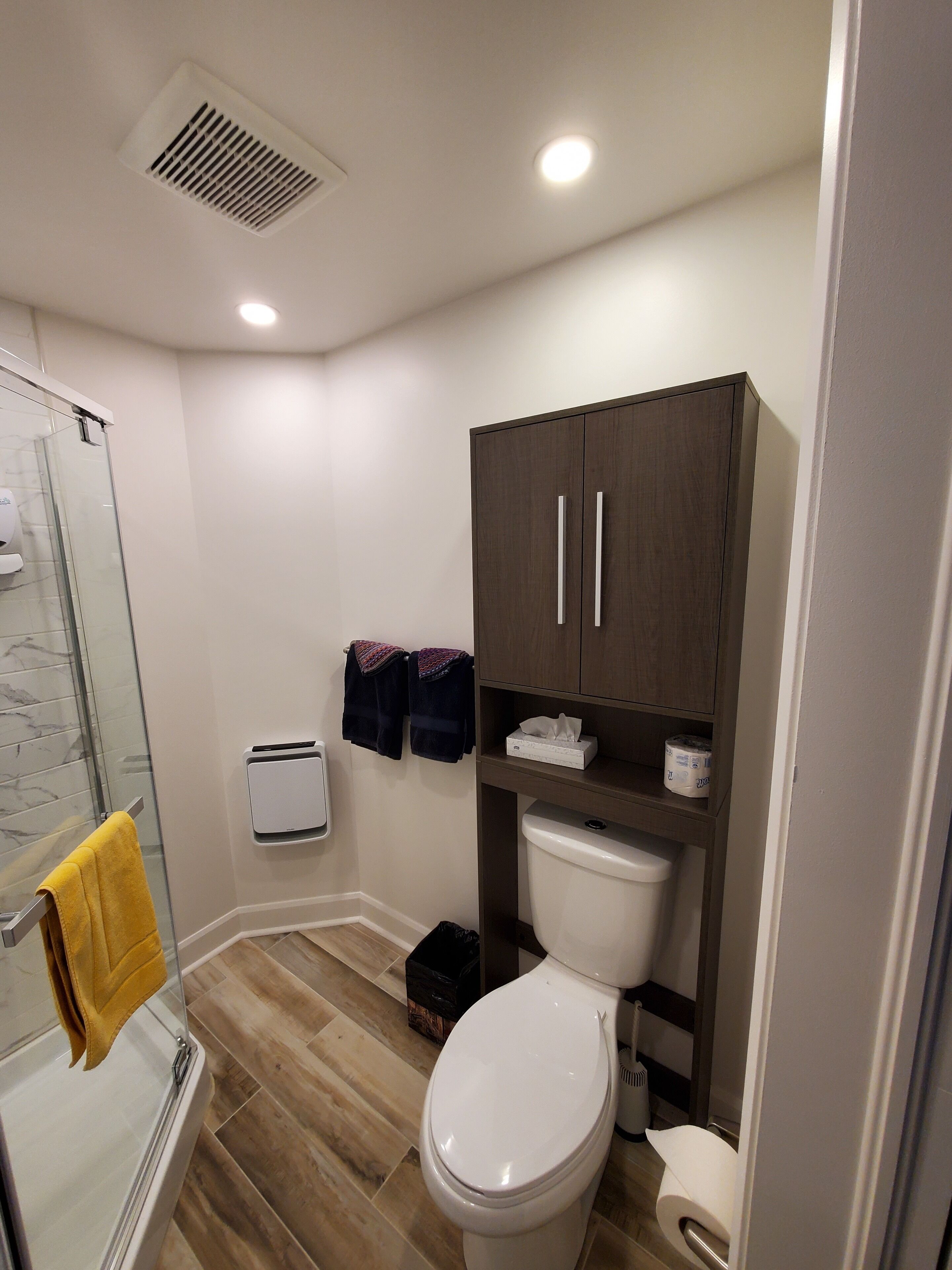 Un baño moderno con cabina de ducha de vidrio, inodoro blanco y mueble oscuro de madera sobre el inodoro.