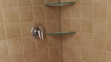 A bathroom with a white bathtub, beige tiled walls, and two glass shelves mounted on the wall.