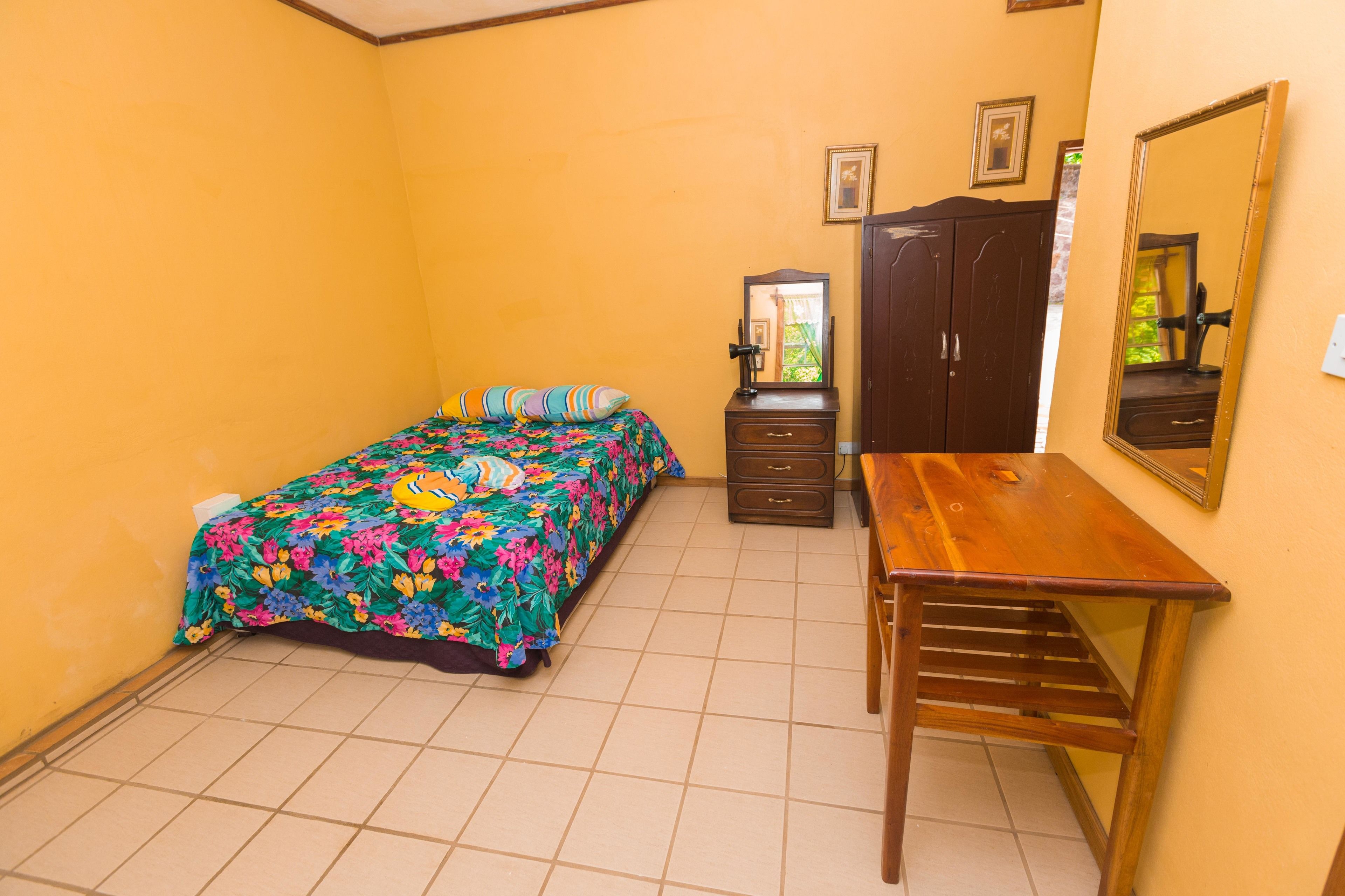 Une chambre à coucher avec un lit, un bureau en bois, une commode et un miroir.