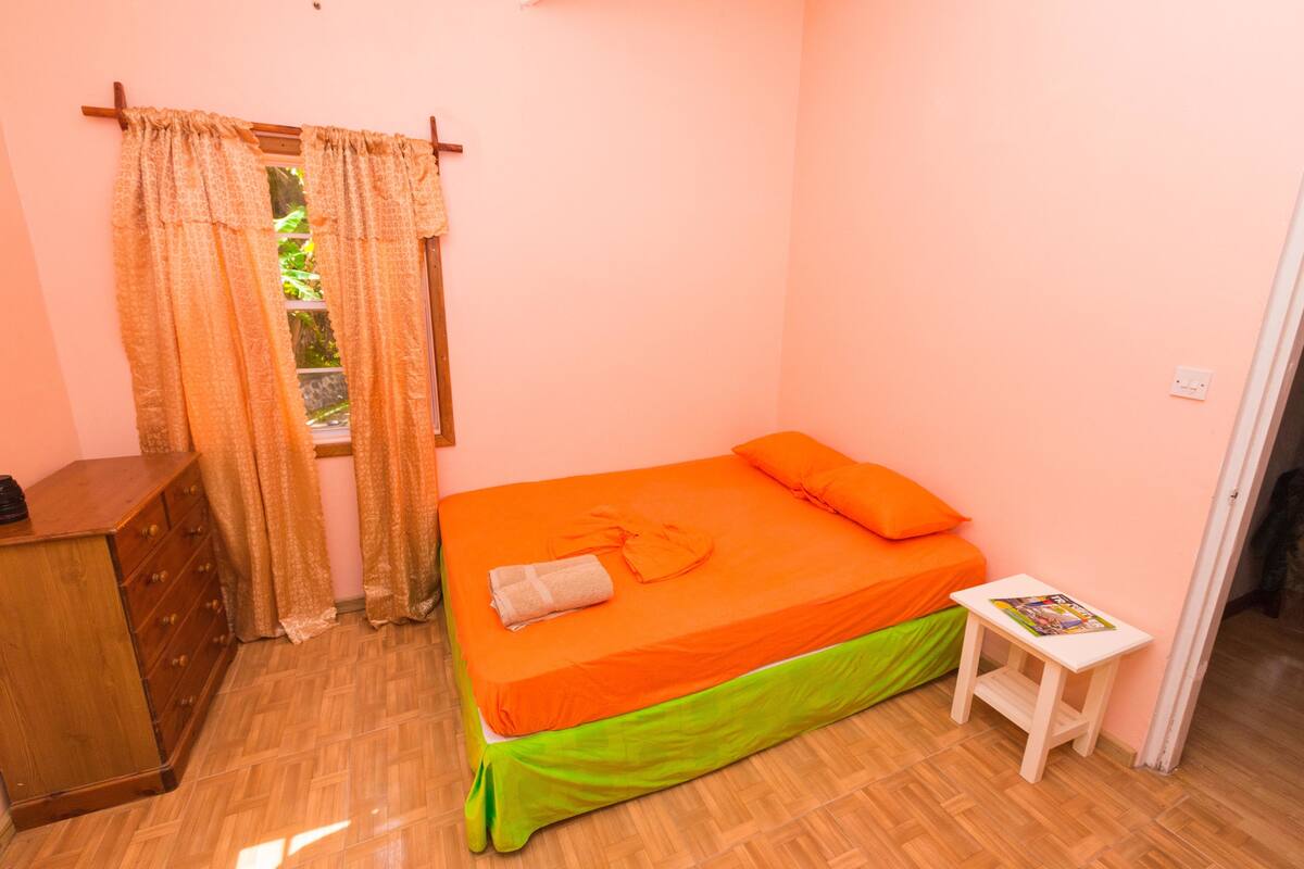 A room with a bed, a small table, a dresser, and a window with curtains.