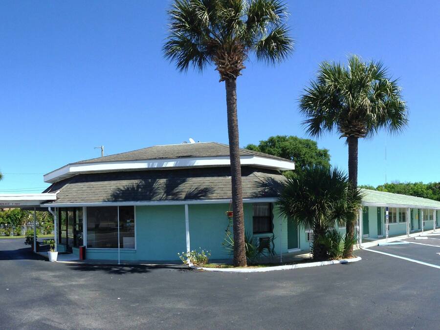 A motel with a clear sign reading "HAWAII MOTEL" and a welcome sign stating "CLEAN & QUIET FREE WIFI HBO WAVE FRIDGE".