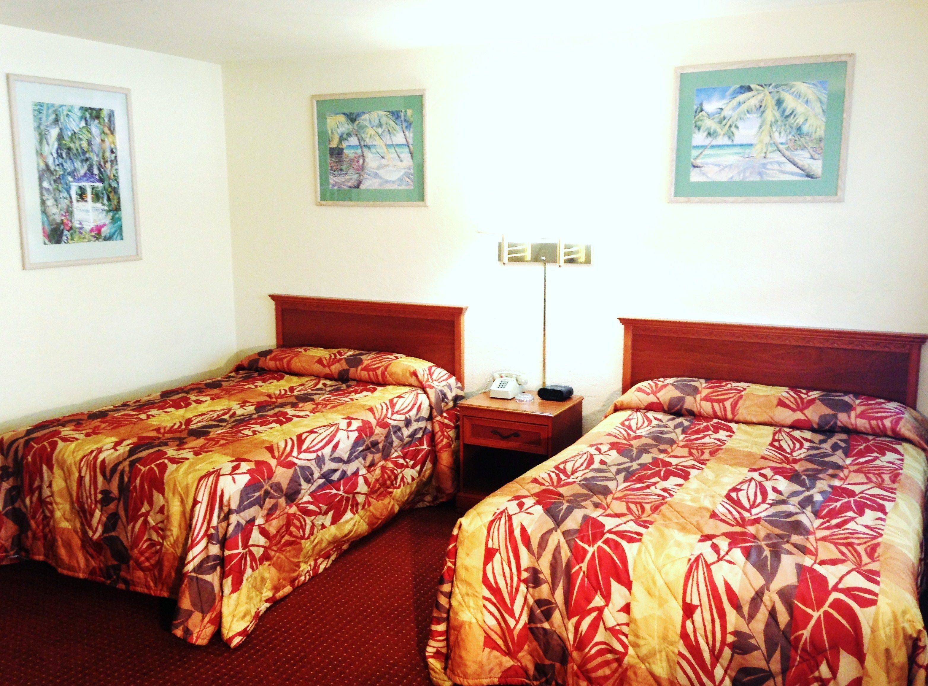 Habitación de hotel con dos camas individuales, una mesita de noche con teléfono y lámpara, y dos cuadros en la pared.