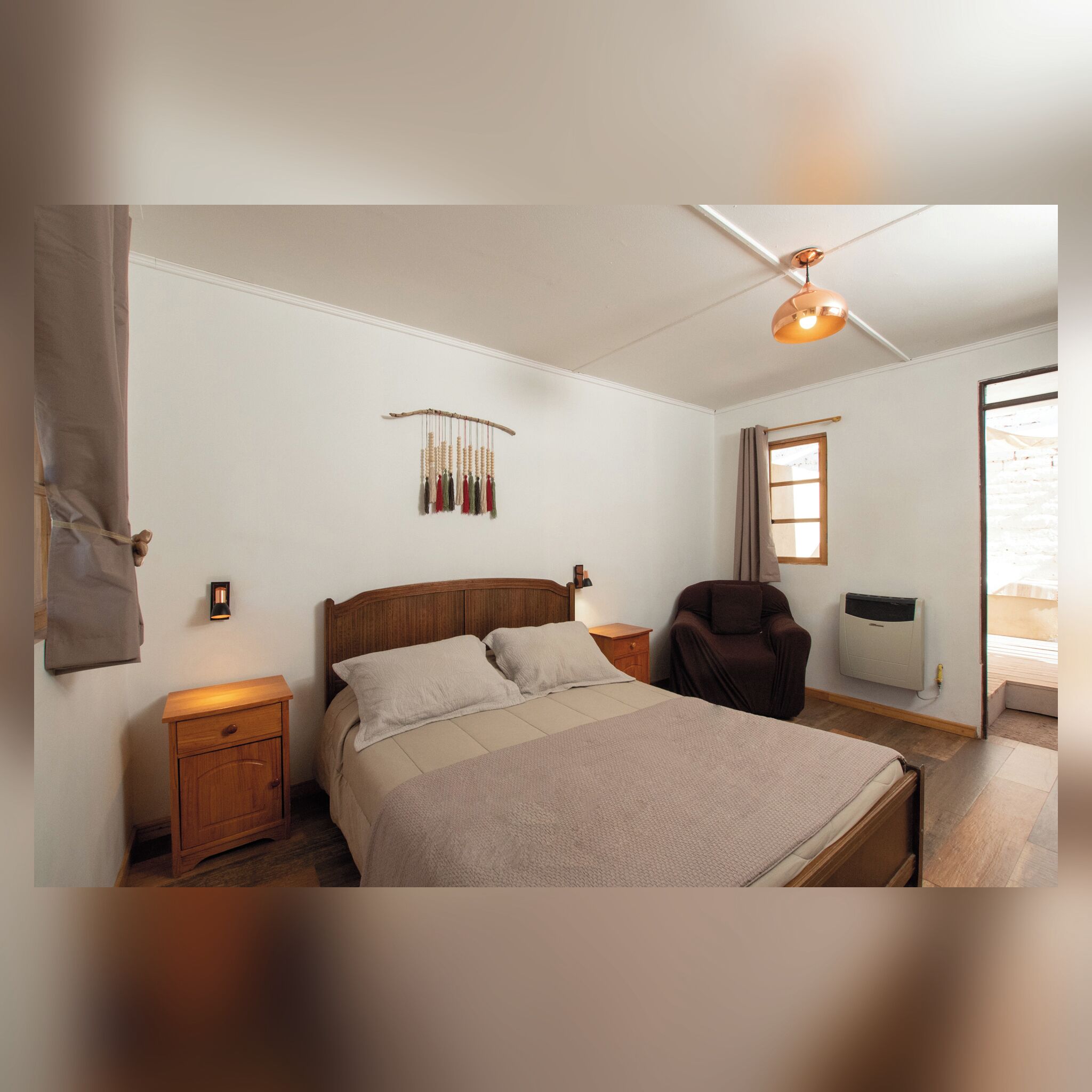 Un dormitorio con cama, mesitas de noche, ventilador de techo, lámpara de pared, ventana y radiador.