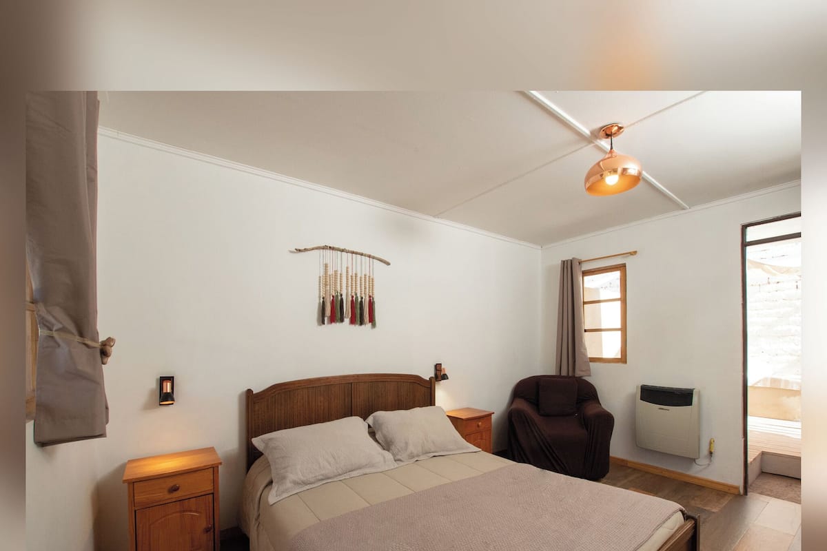Un dormitorio con cama, mesitas de noche, ventilador de techo, lámpara de pared, ventana y radiador.