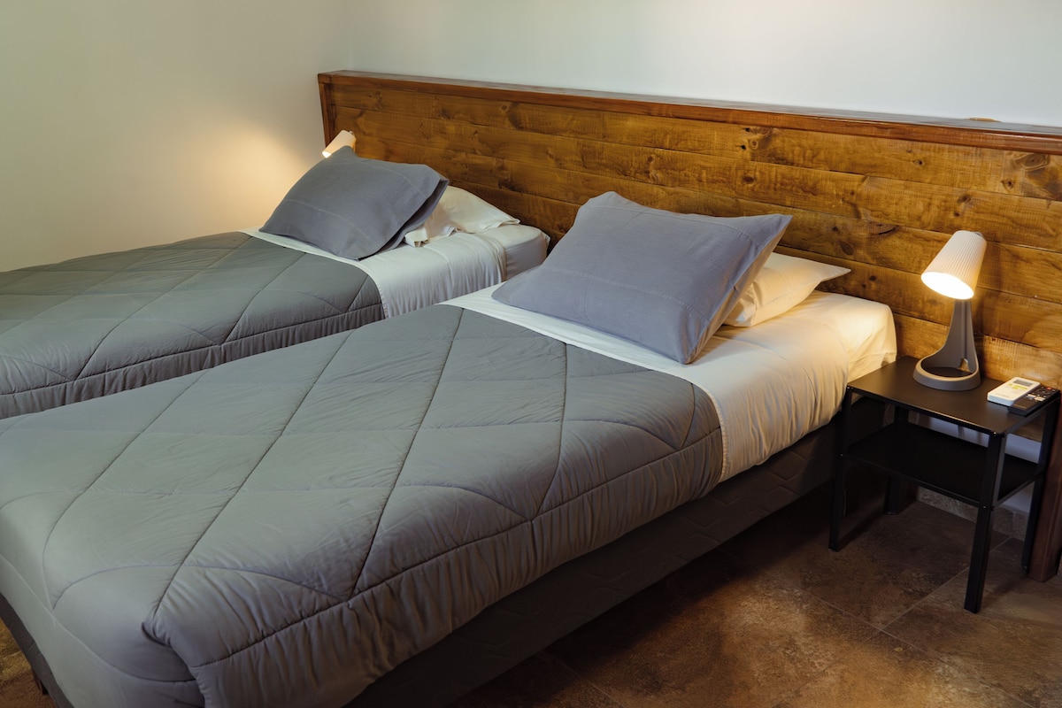Una cama doble con cabecera de madera, una mesita de noche con lámpara y un cuadro colgado en la pared.