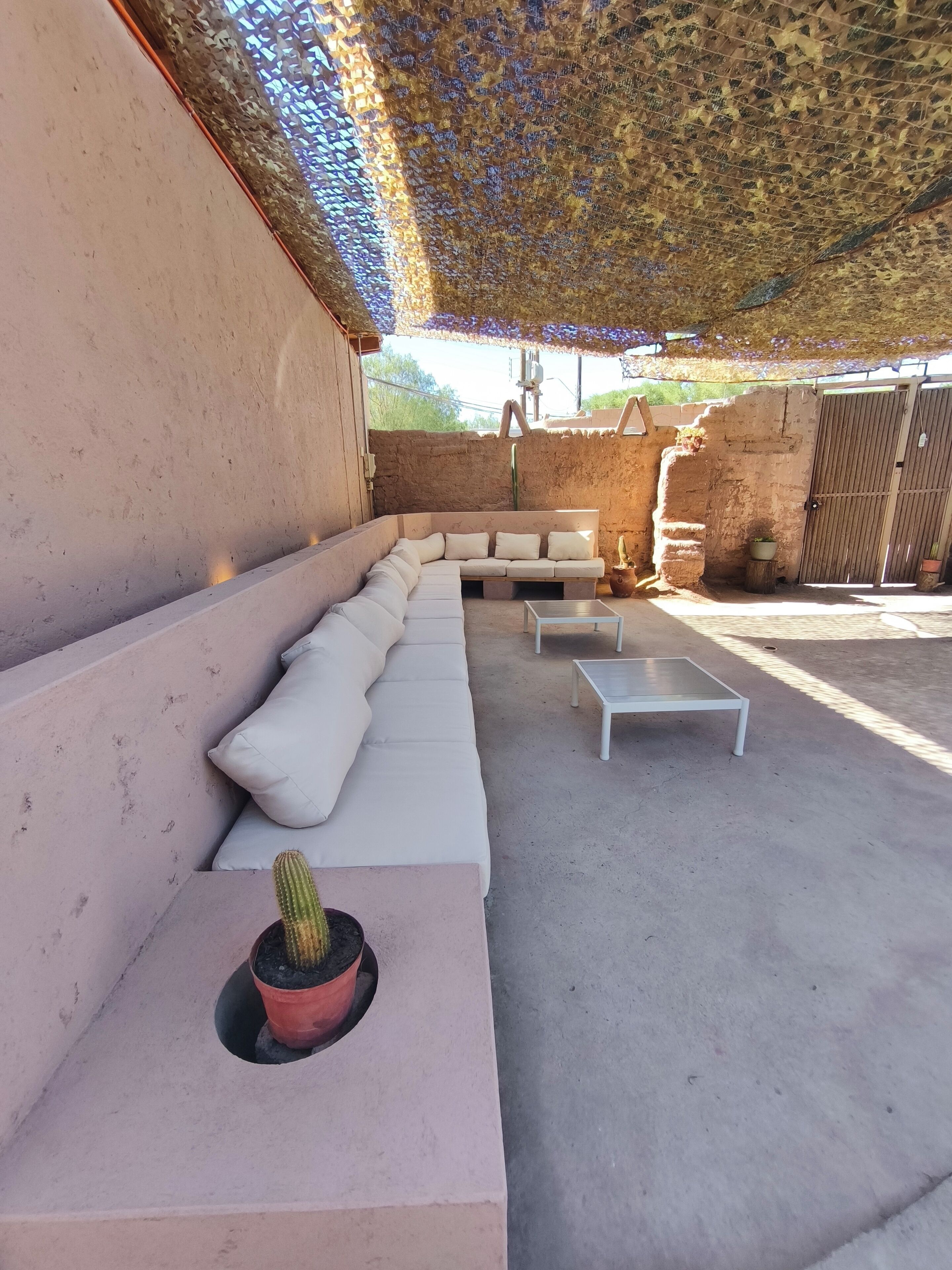 Un espace extérieur aménagé avec un long canapé blanc, deux petites tables et un cactus en pot.