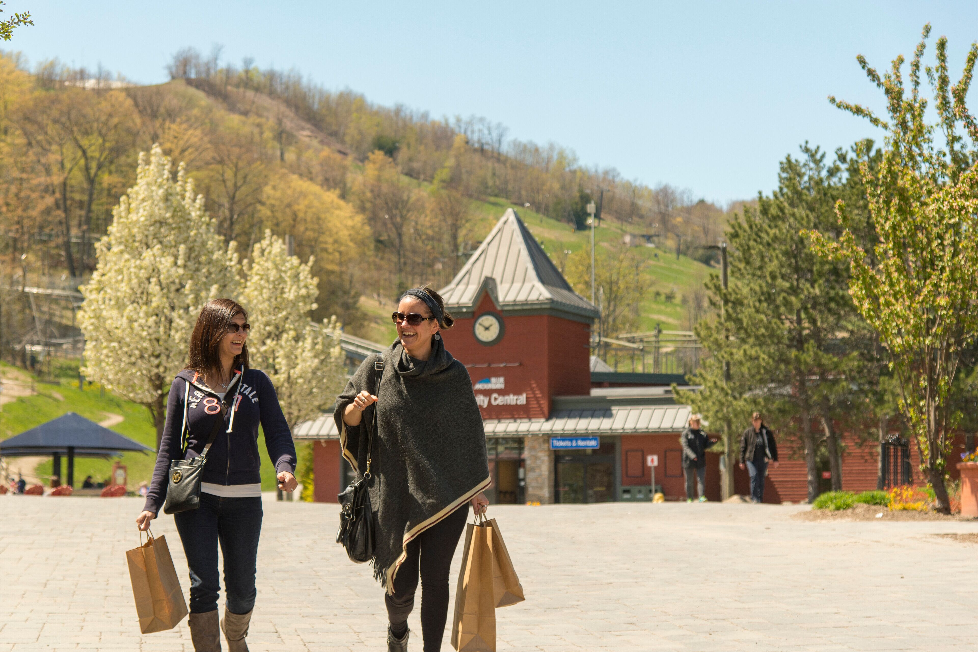 Two people walking in a public square with a clock tower and a building labeled "City Central" in the background.