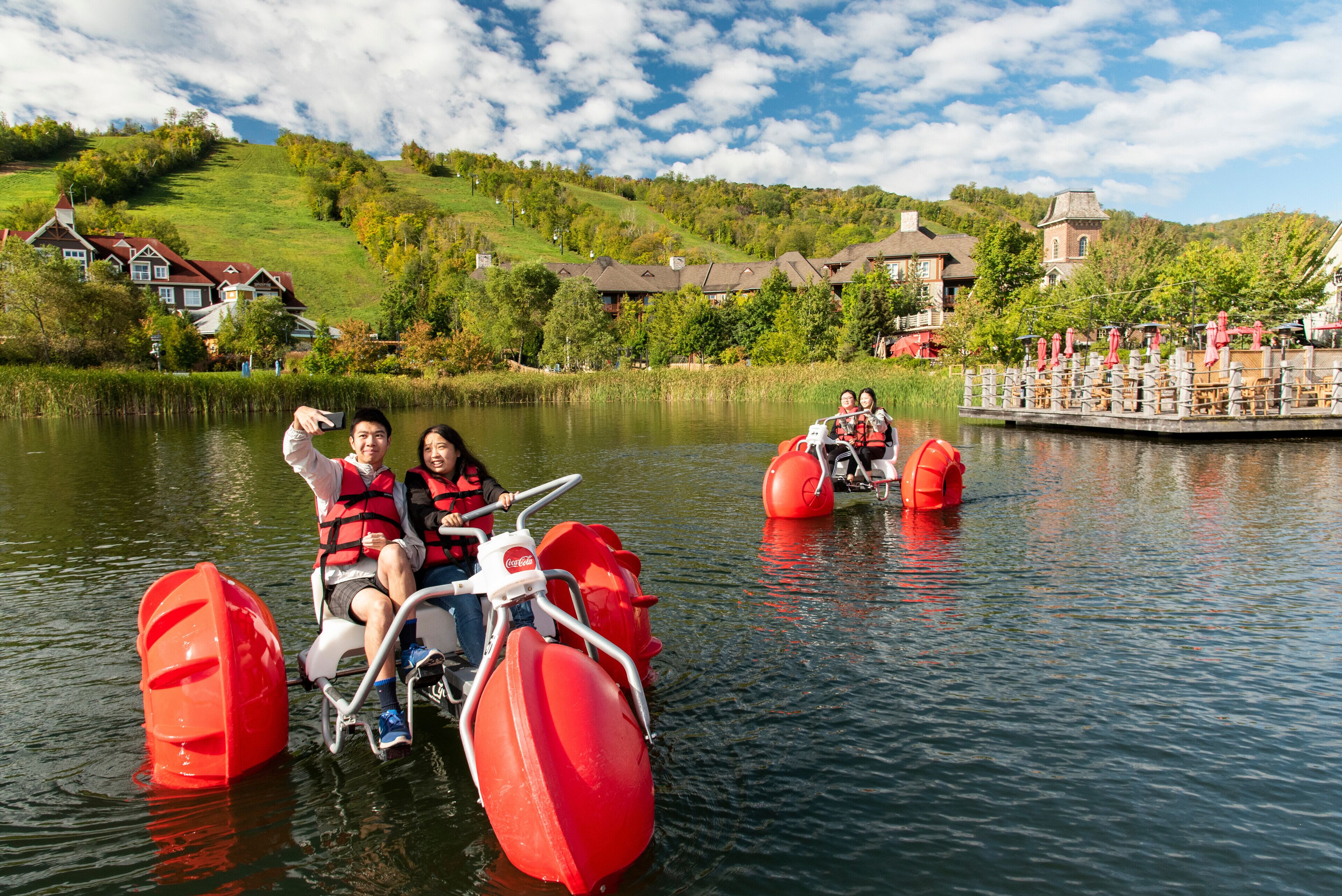 Um lago com pedalinhos, um píer com guarda-sóis e casas ao fundo.
