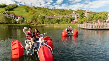 Um lago com pedalinhos, um píer com guarda-sóis e casas ao fundo.