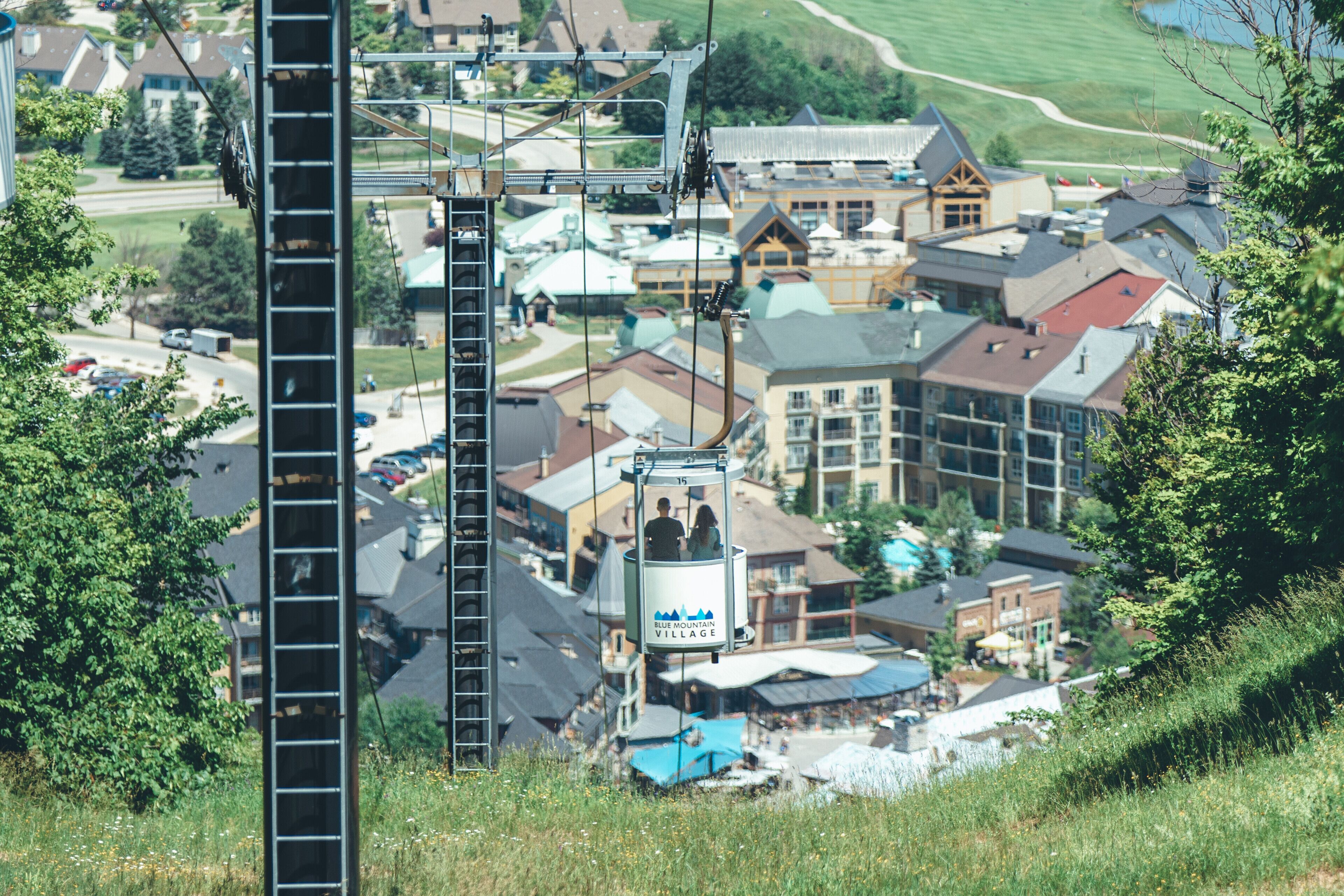 Sistema de teleférico con una cabina identificada como “Blue Mountain Village” en medio de un pueblo con diversos edificios y una ladera.