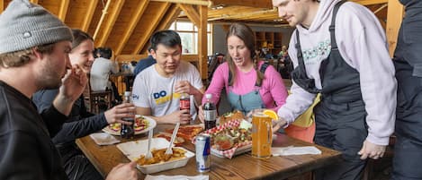 A group of people dining at a wooden table with food and drinks.