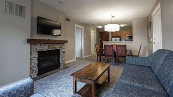 A living room with a stone fireplace, a flat-screen TV, a wooden coffee table, and a blue sofa.