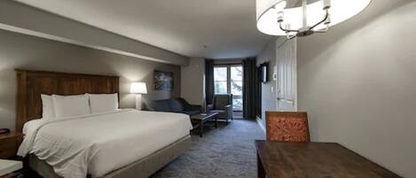 A hotel room with a large bed, a desk, a chair, a lamp, and a view of the outdoors.