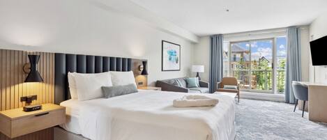 A modern hotel room with a large bed, a desk, a chair, and a balcony with a view.