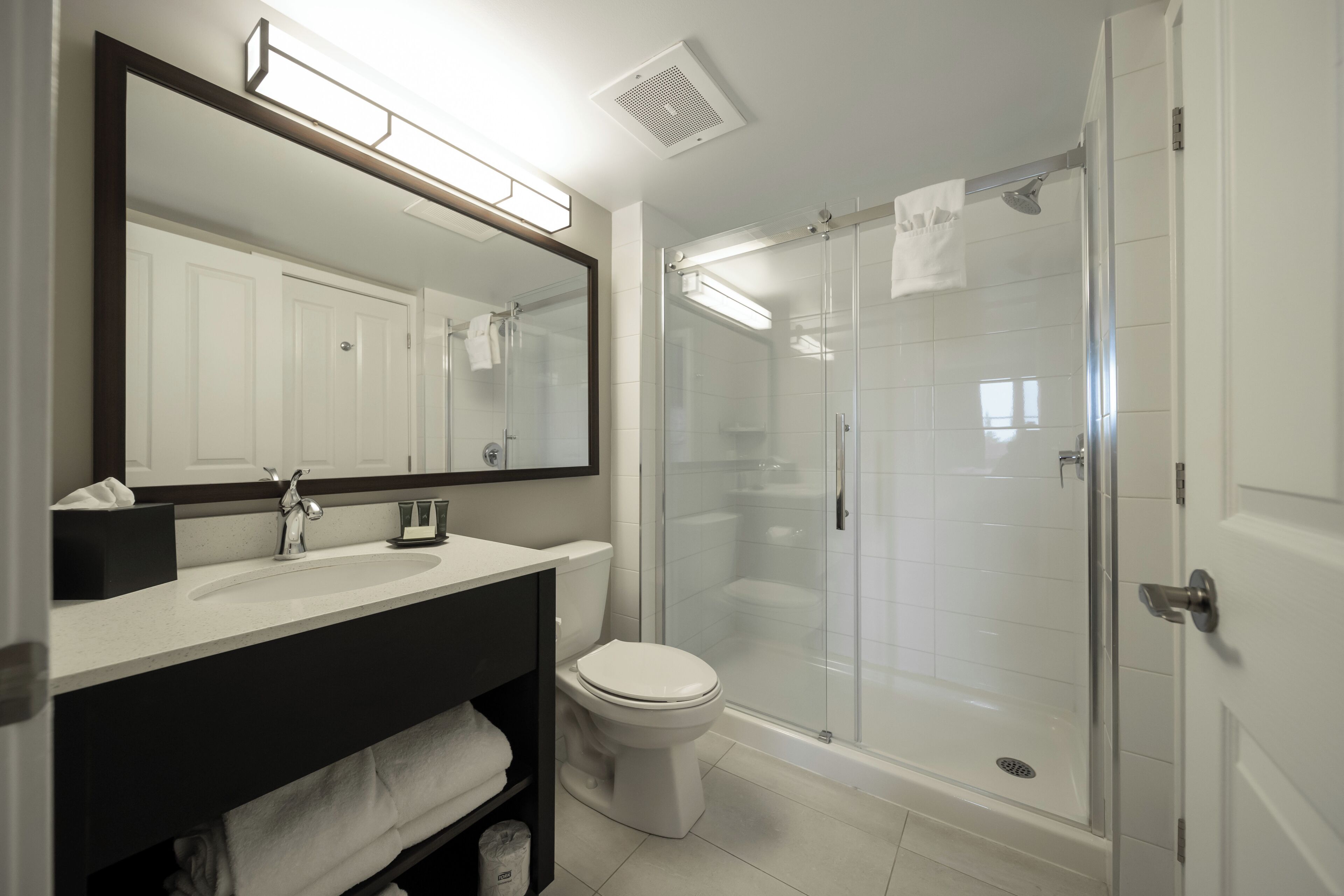 A modern bathroom with a white sink, a toilet, a glass-enclosed shower, and a large mirror.